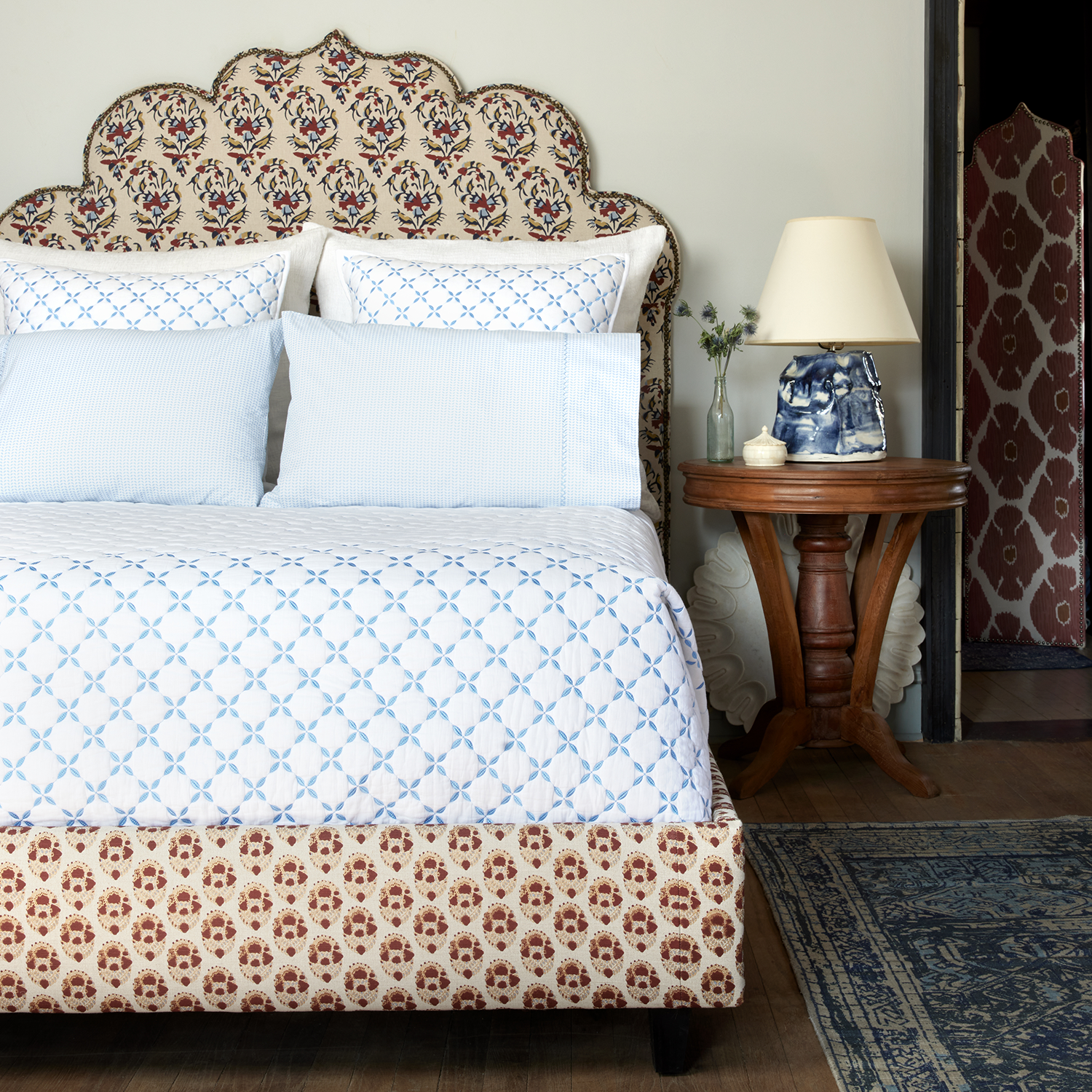 A bed with a Layla Azure Quilt headboard made of cotton voile from John Robshaw.