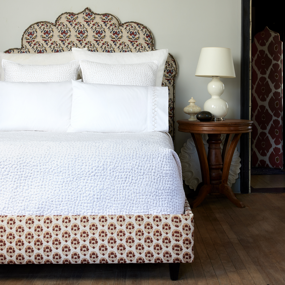 A white bed with an ornate headboard made of John Robshaw's Organic Hand Stitched Sand Quilt.