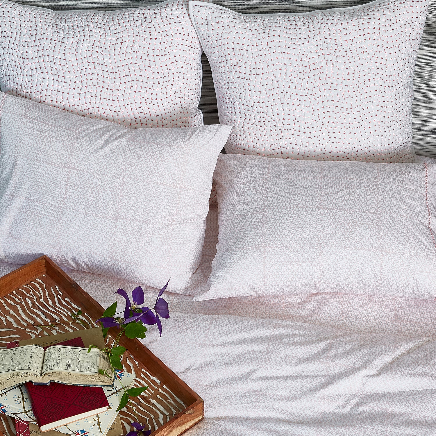 A cozy bed with John Robshaw's Organic Hand Stitched Lotus Quilt pillows and a book on top.