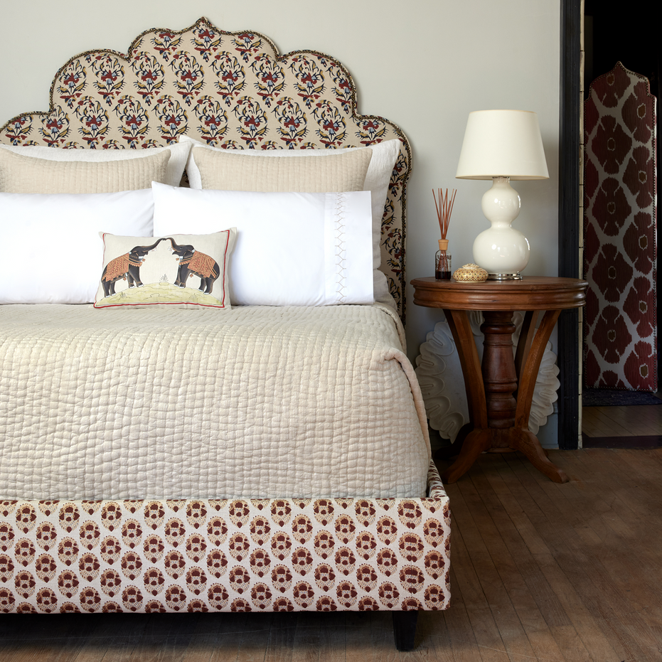 A bed with a patterned headboard adorned with John Robshaw's Vivada Sand Woven Quilt coverlets.