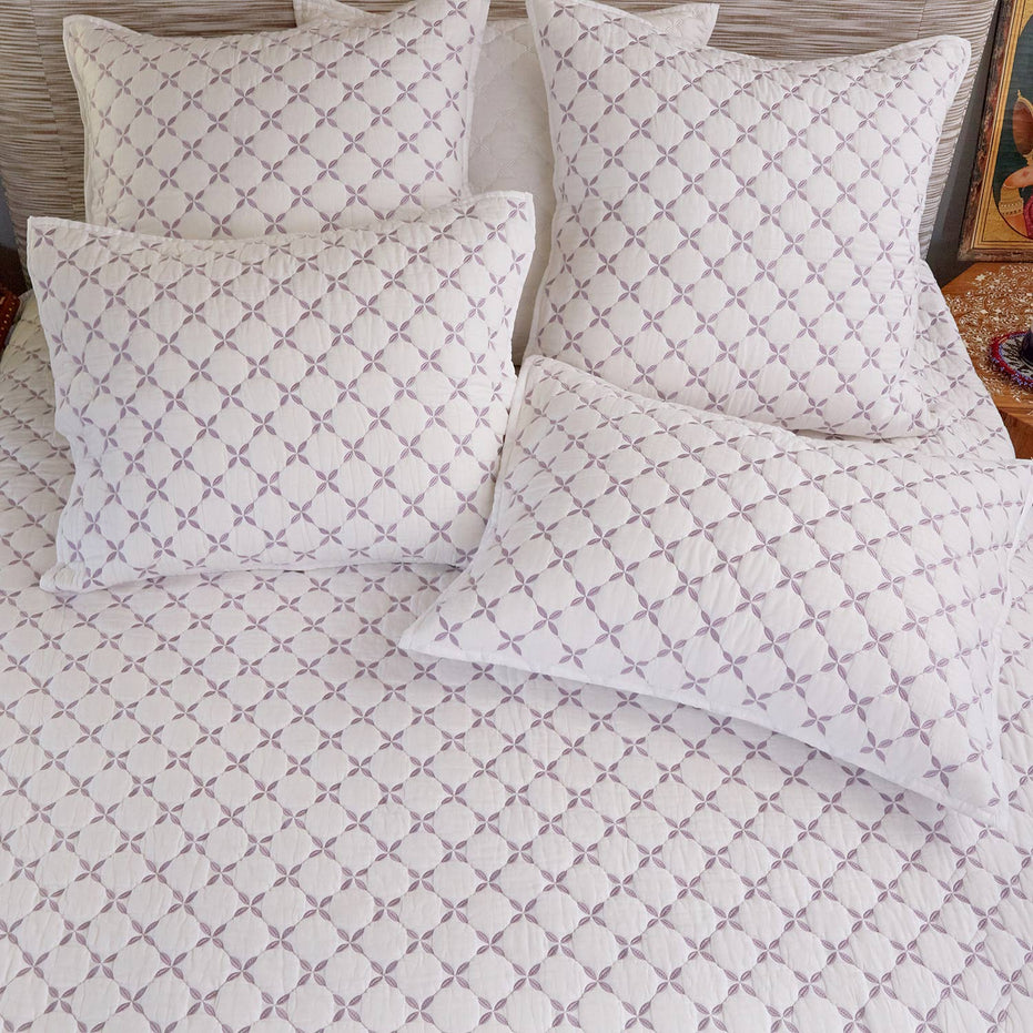 A bed featuring a Layla Lavender Quilt by John Robshaw, adorned with matching pillows.
