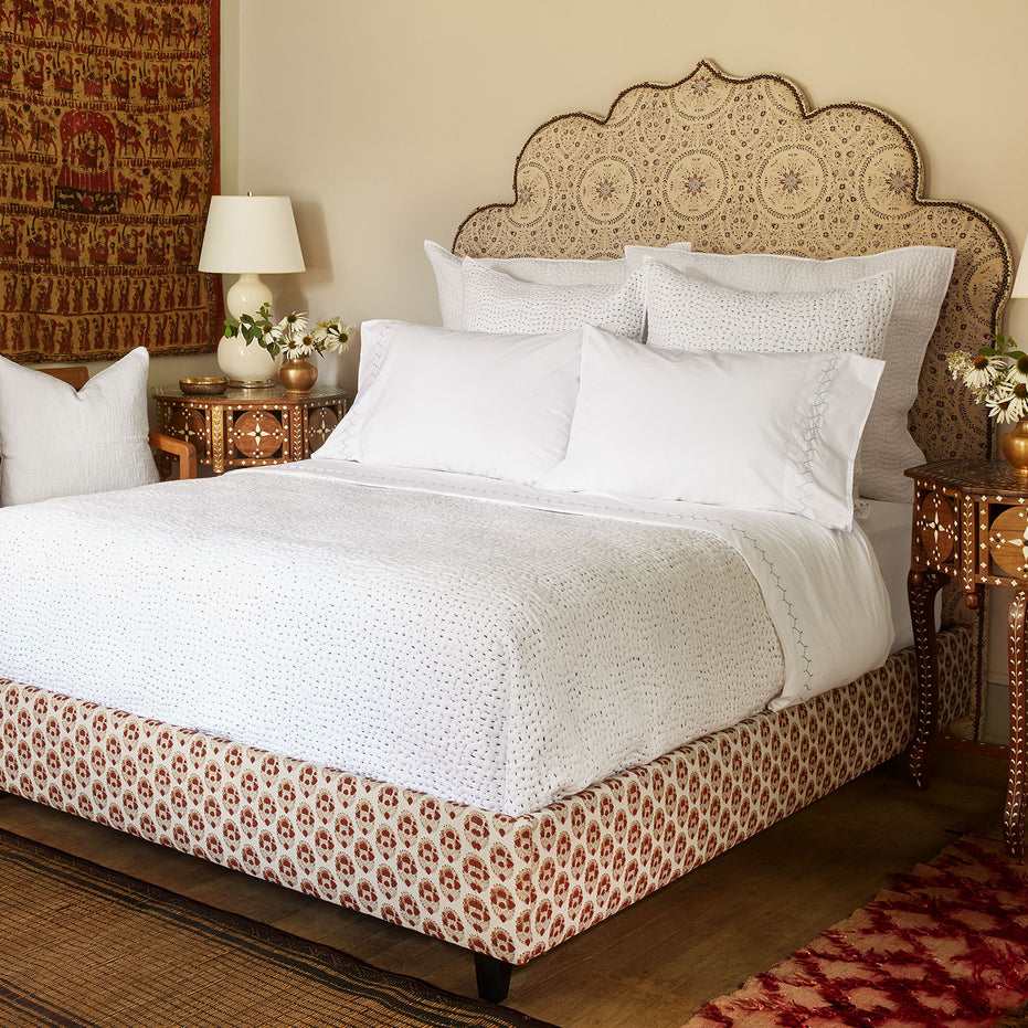 A John Robshaw Custom Bihar Bed with an ornate headboard, covered in fabric, in a bedroom.