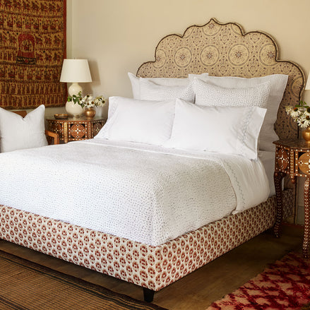 A John Robshaw Custom Bihar Bed with an ornate headboard, covered in fabric, in a bedroom.